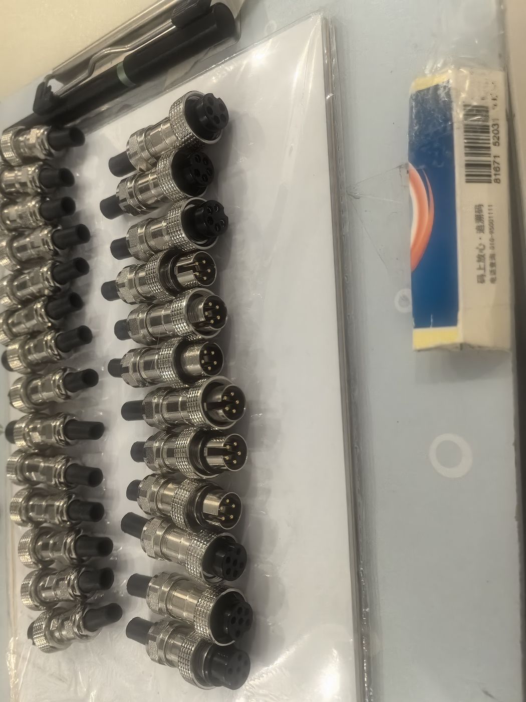 Metal circular connectors laid out in rows on a white tray with a small blue box alongside