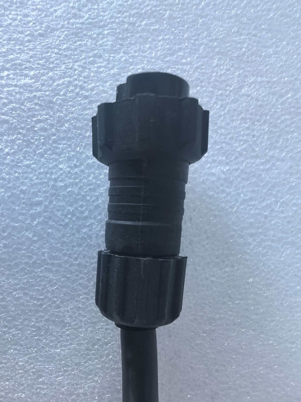 A black two-pole waterproof connector on the end of a black cable against a pale blue background