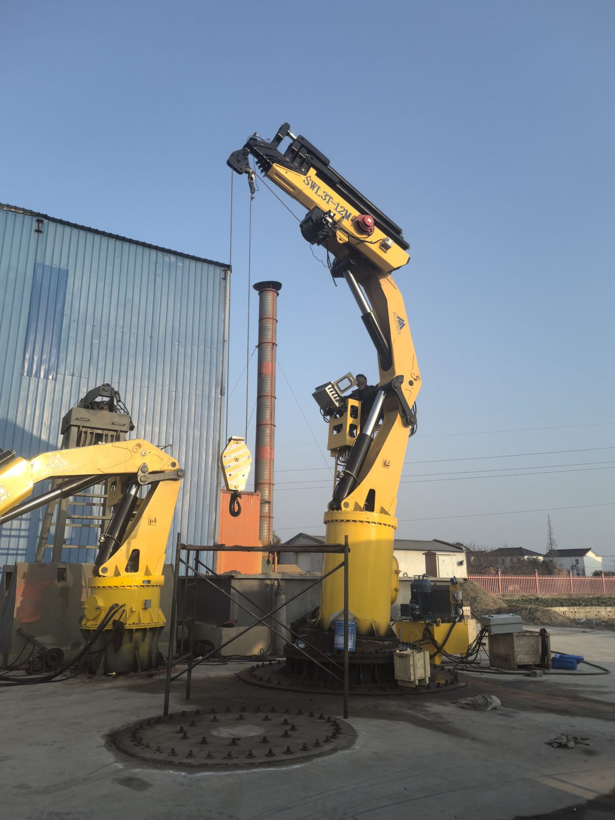 Two yellow knuckle boom cranes standing in a yard at dusk