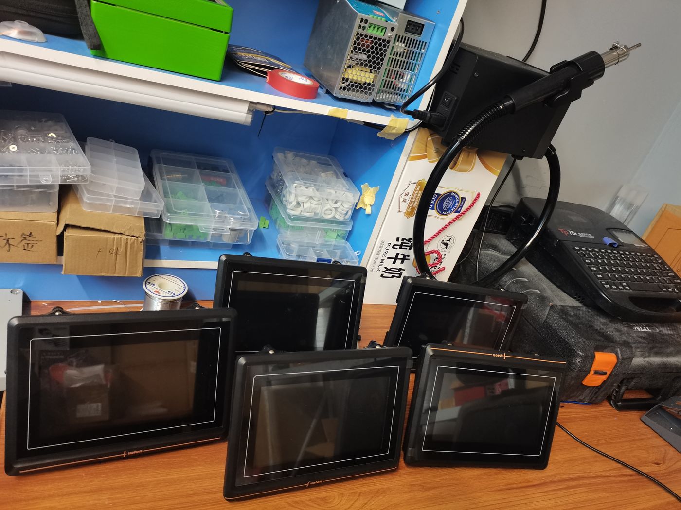 Five black terminal faces of different sizes standing on a workbench, parts bins and a soldering station behind
