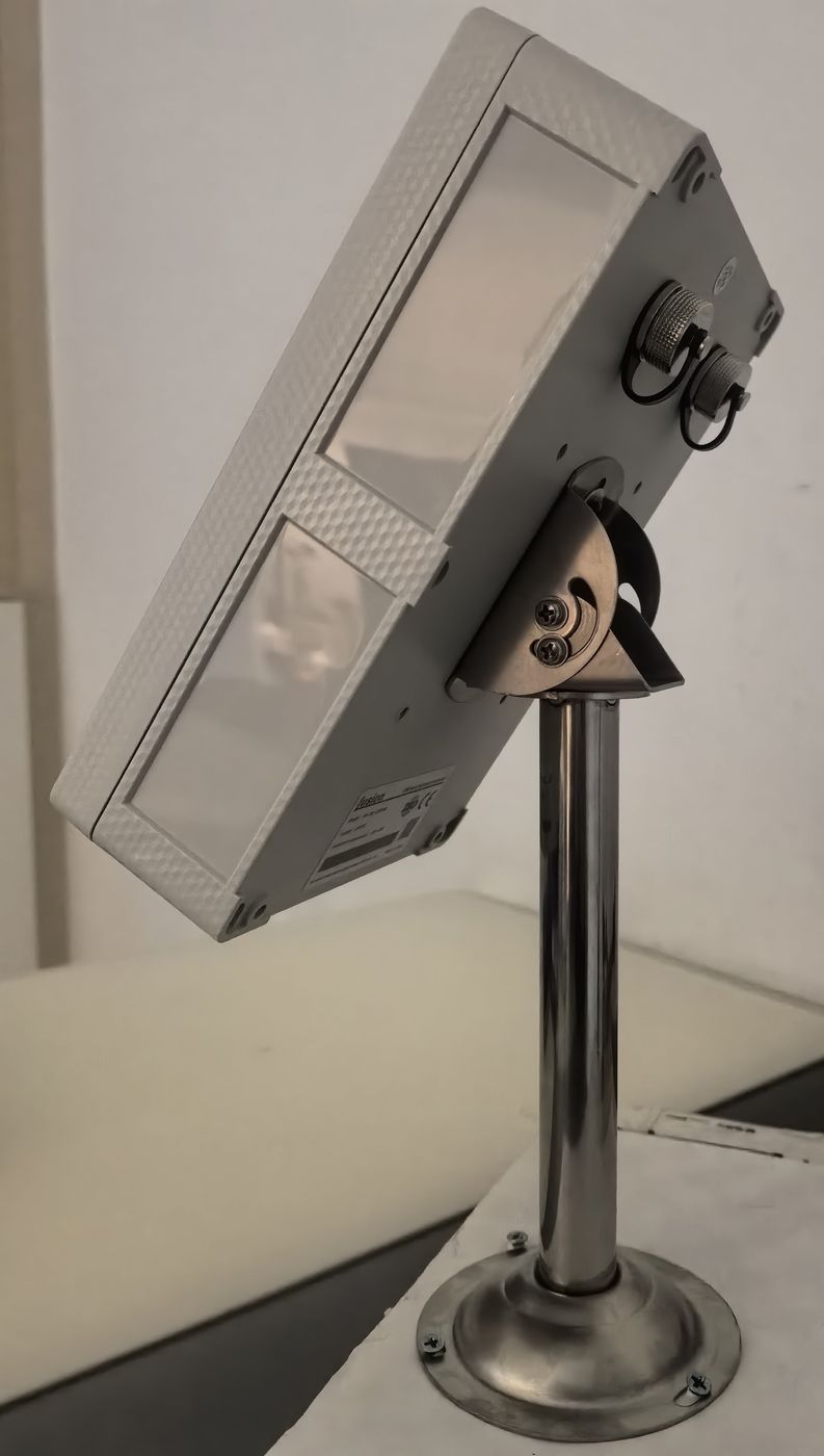 Grey control box seen from behind, mounted on a metal pedestal with two lever seats and the cable entry visible