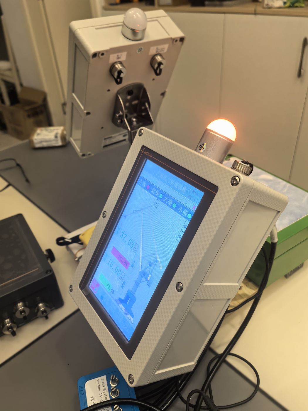 An amber beacon lit on the grey control box above a terminal showing a blue work screen