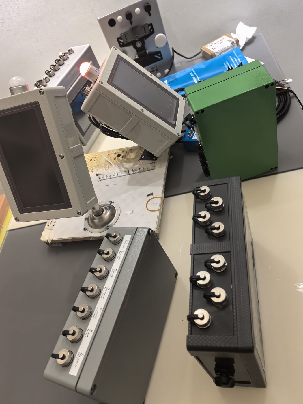 Two pedestal-mounted grey terminals, a green enclosure and two junction strips with knobs, black and grey, on a bench