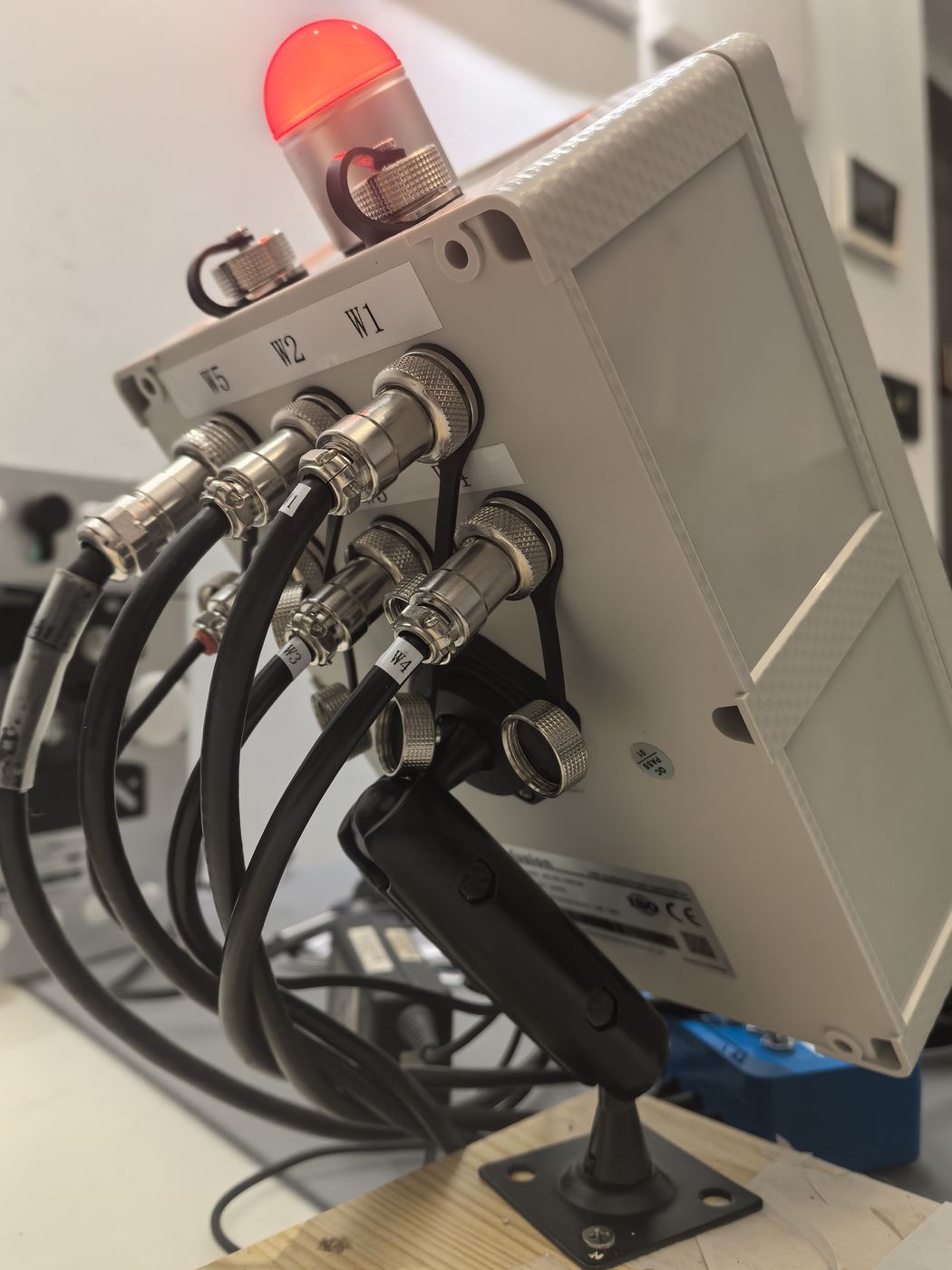 Back of a grey terminal housing with a red beacon on top, a row of metal glands taking coiled cables and a black lever below