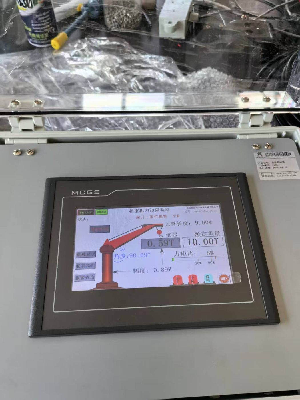 A grey terminal face lying flat, screen showing a red crane graphic with readouts, bubble wrap and parts behind