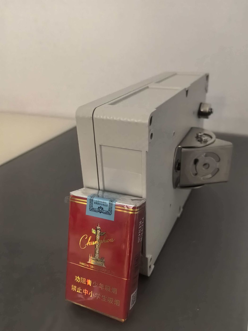 Grey host housing standing upright with a metal bracket on its side and a small red box in front for scale