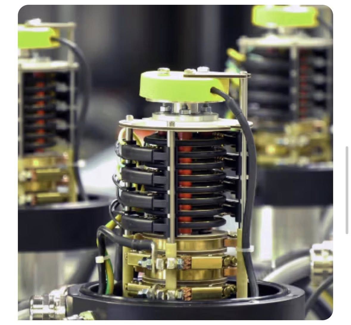 A slip ring with its housing removed, showing stacked copper tracks and black brush assemblies under a green flange