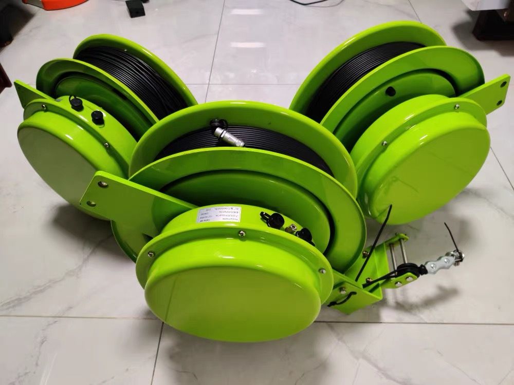 Three green draw-wire reels standing side by side on tiles with black cord led out at the side