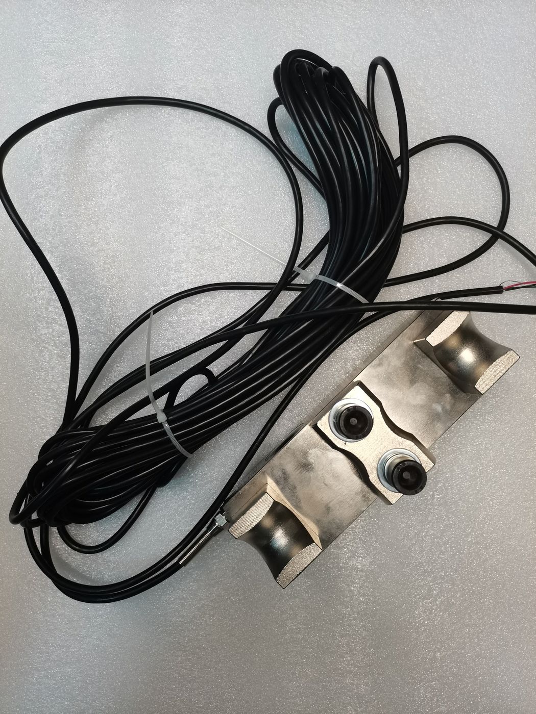 A large coil of black cable and a two-bore bending flexure cell on a grey floor