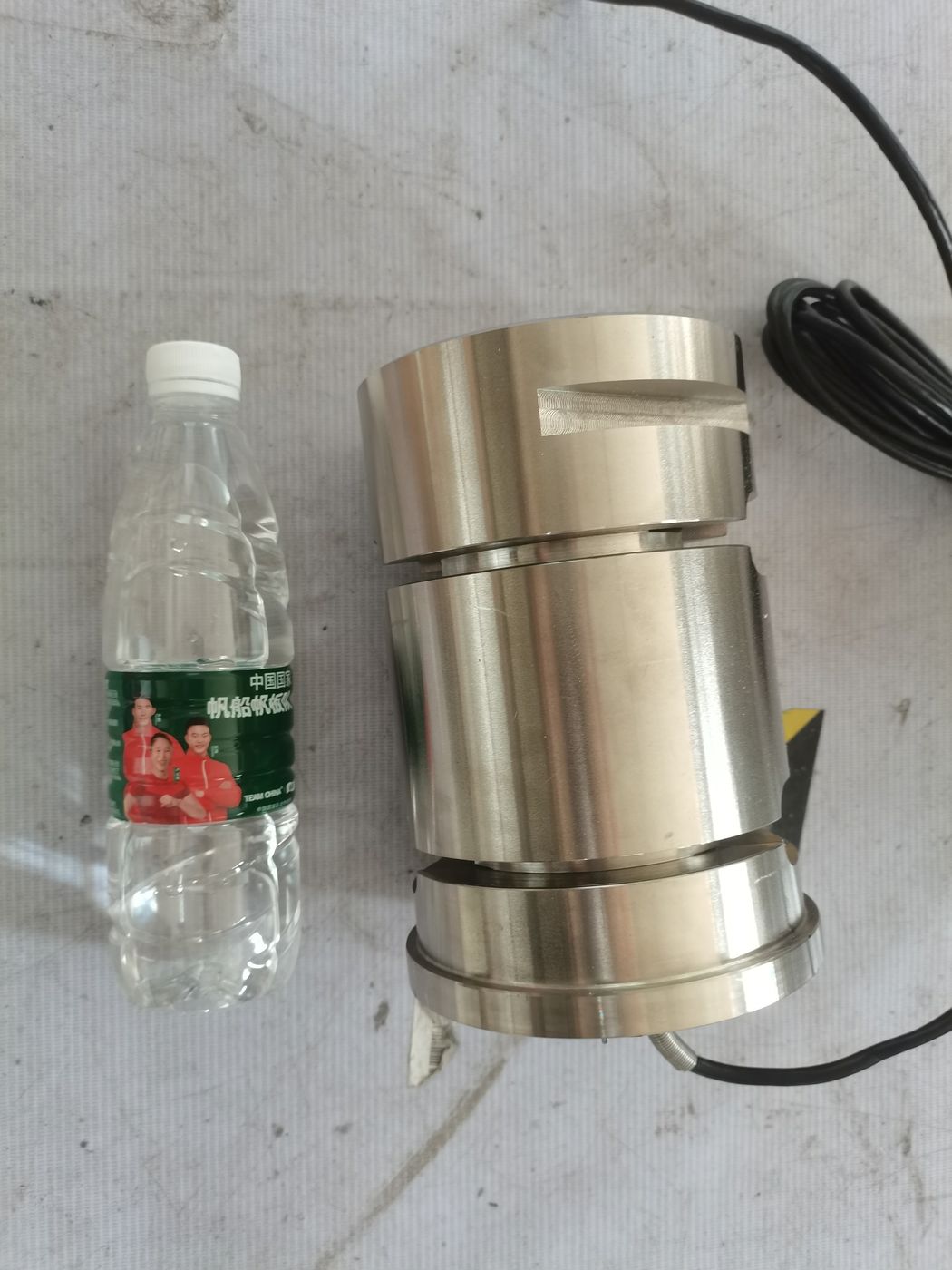 Two stainless ring-type cells side by side on a white surface with a water bottle at left for scale
