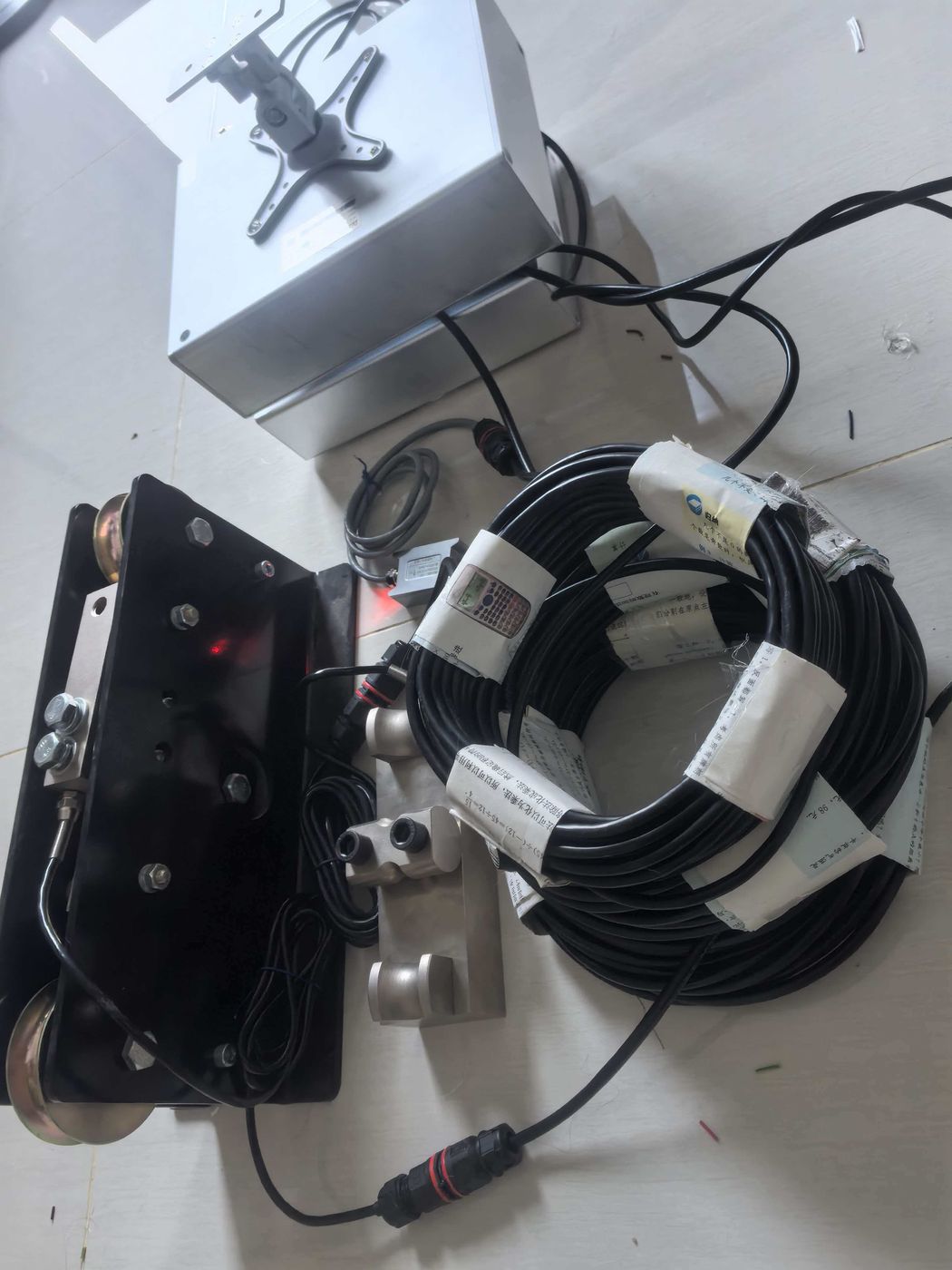 Silver collector box, black sheave frame and two cable coils with white tags on a white floor