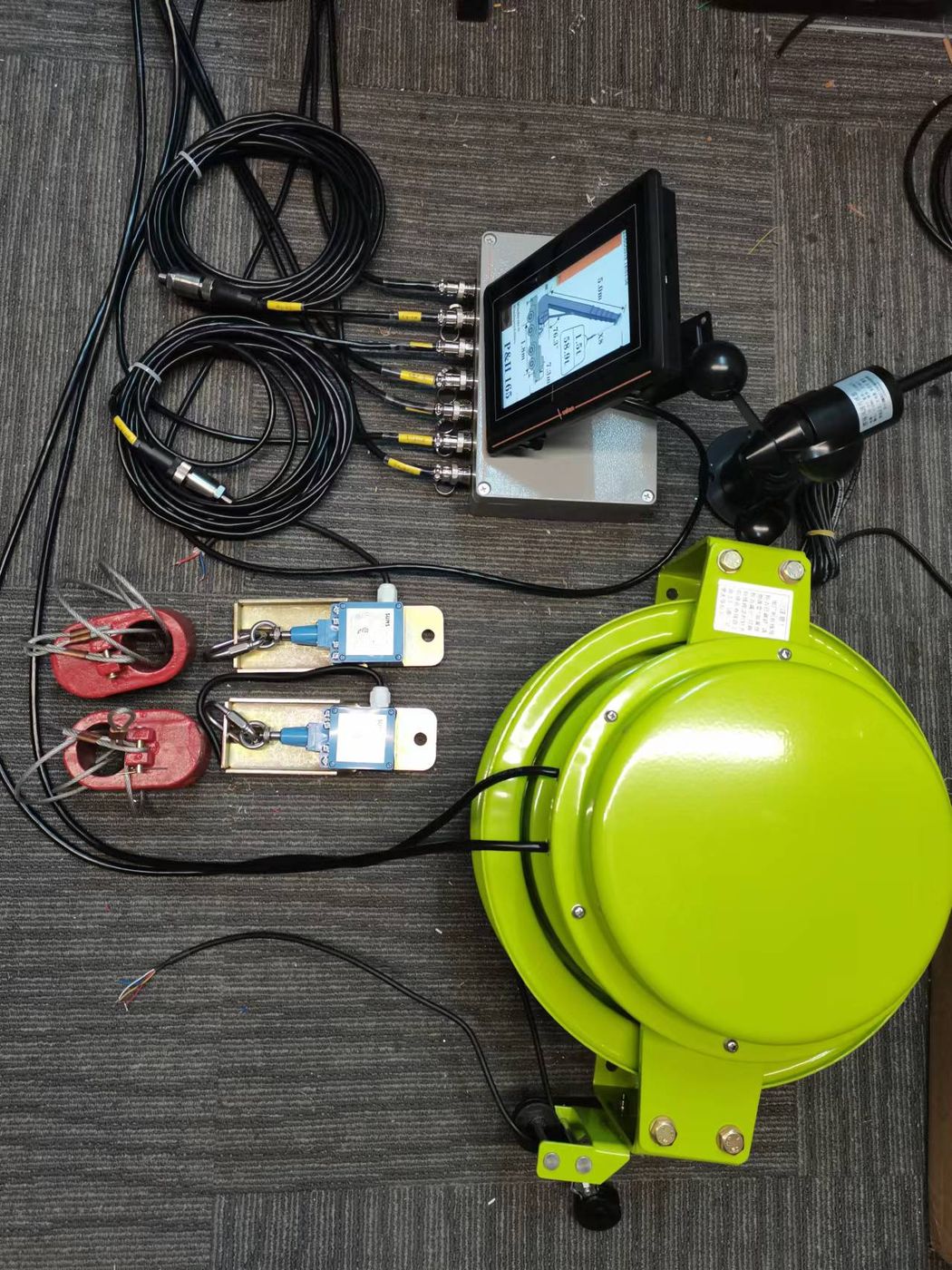 A terminal, a green draw-wire reel, two pin-type cells and coiled cable laid out on office carpet