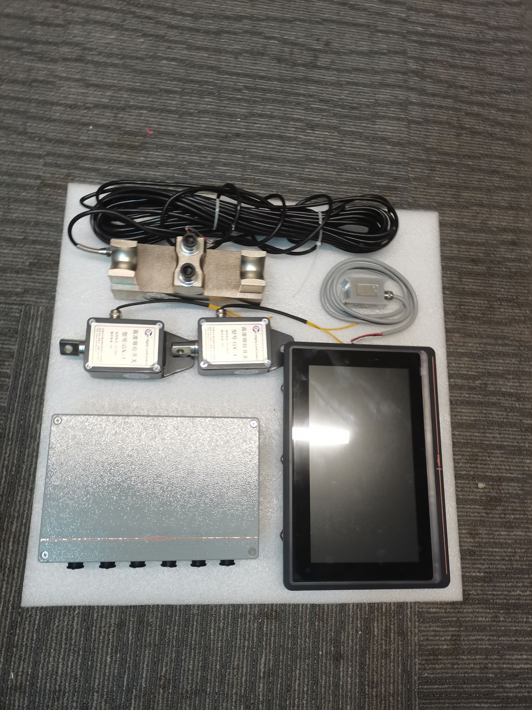 Collector box, a black terminal, two labelled cells and cable arranged on a white foam board