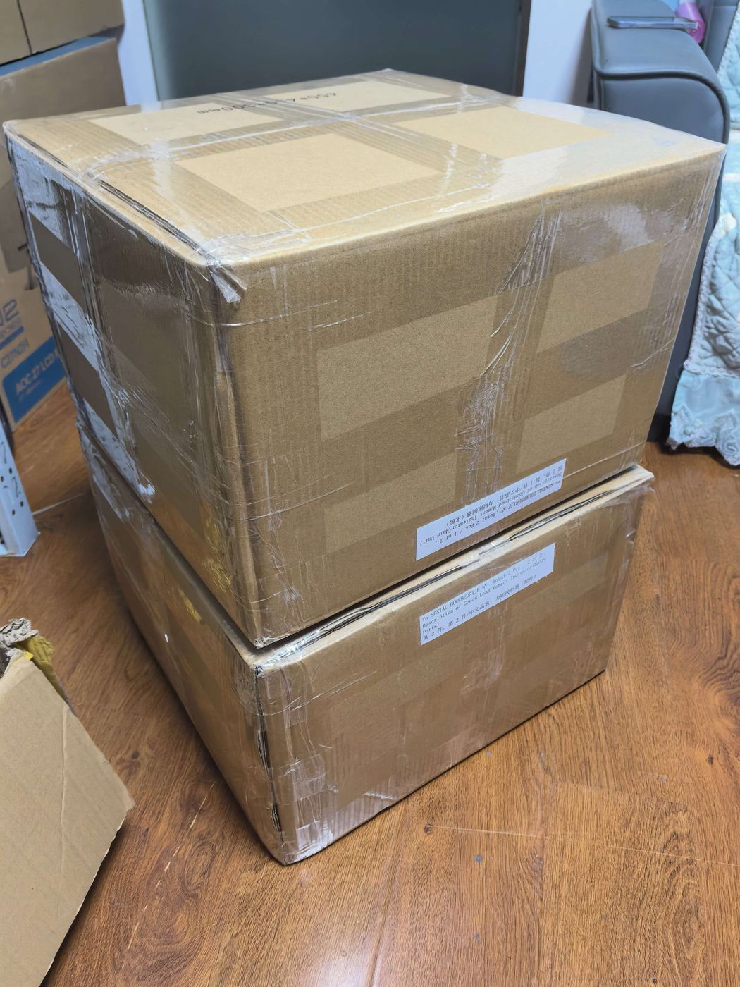 Two cartons stacked on a wooden floor, wrapped clear with tape