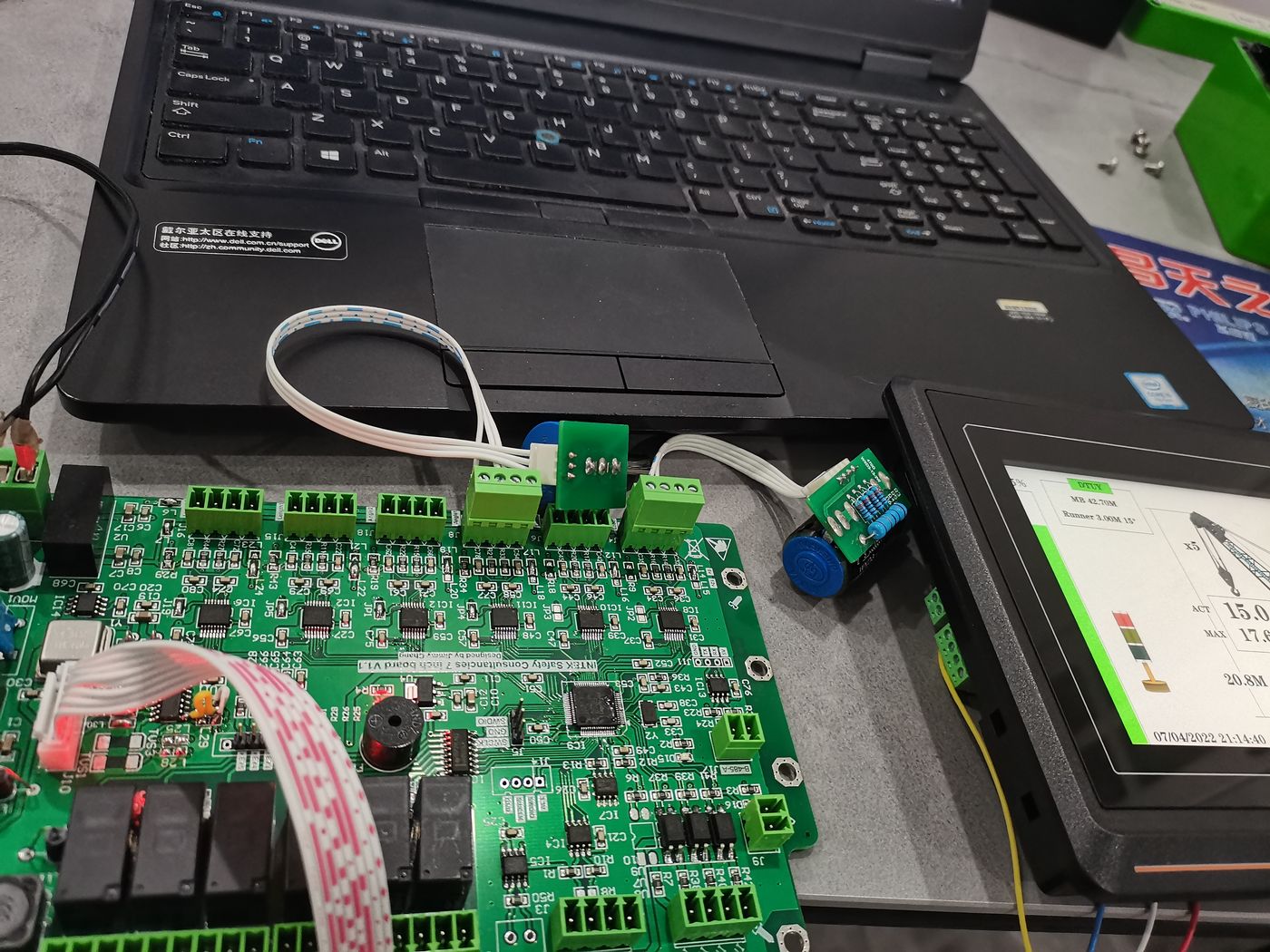 Green collector board beside a laptop with ribbon and terminal wiring landed, a terminal showing channel pages to the right