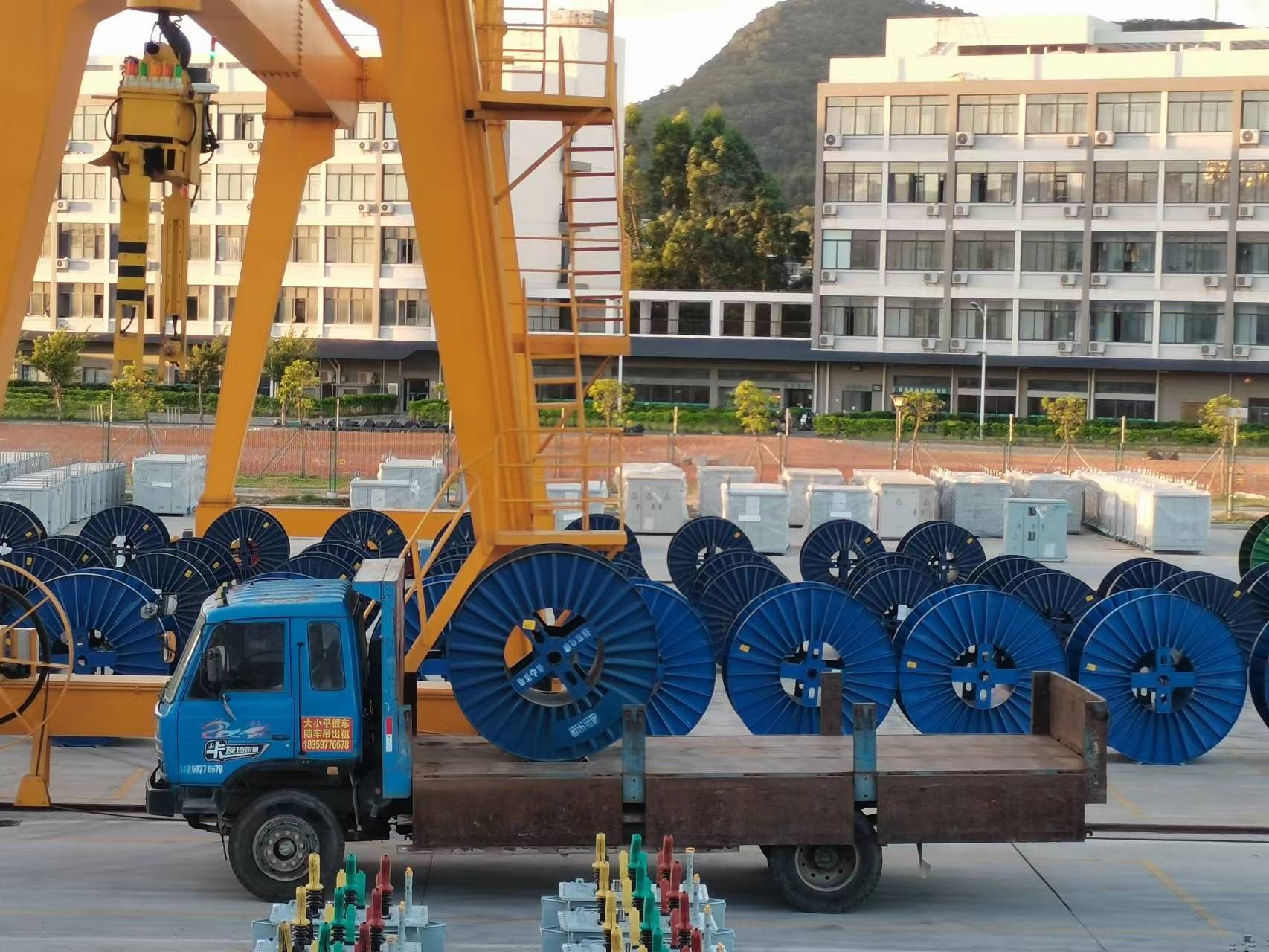Truck loaded with blue cable reels beside a yellow crane structure