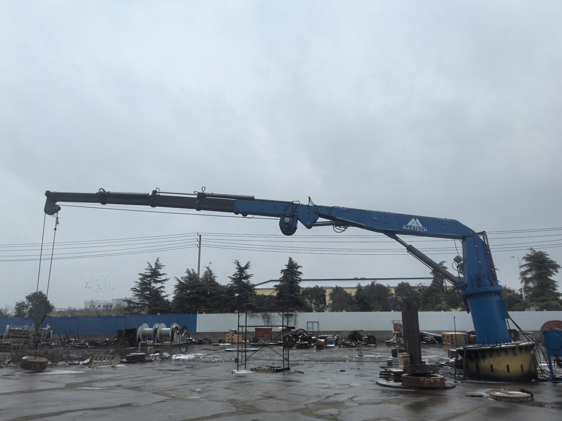 Blue truck-mounted crane with a luffing jib in a working yard