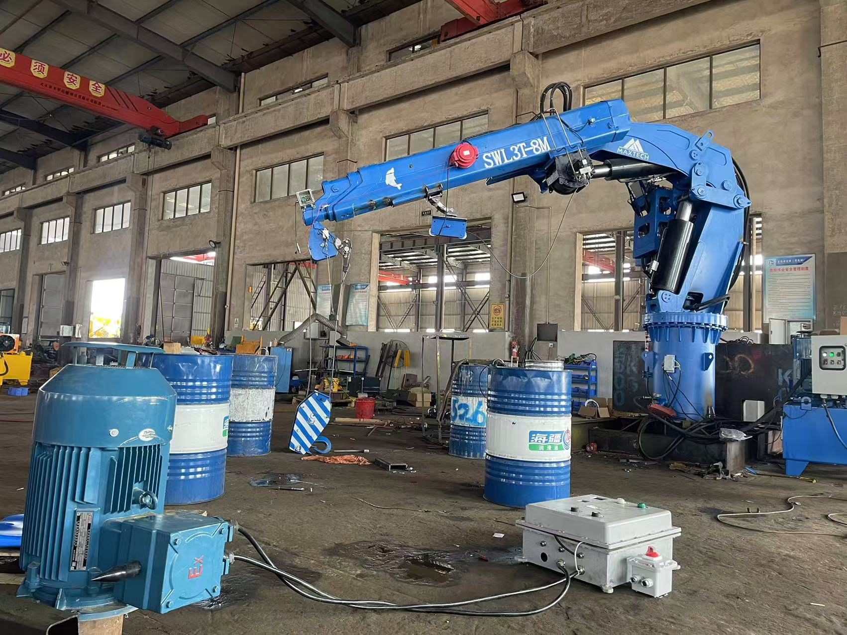 Blue articulating crane moving drums inside a workshop