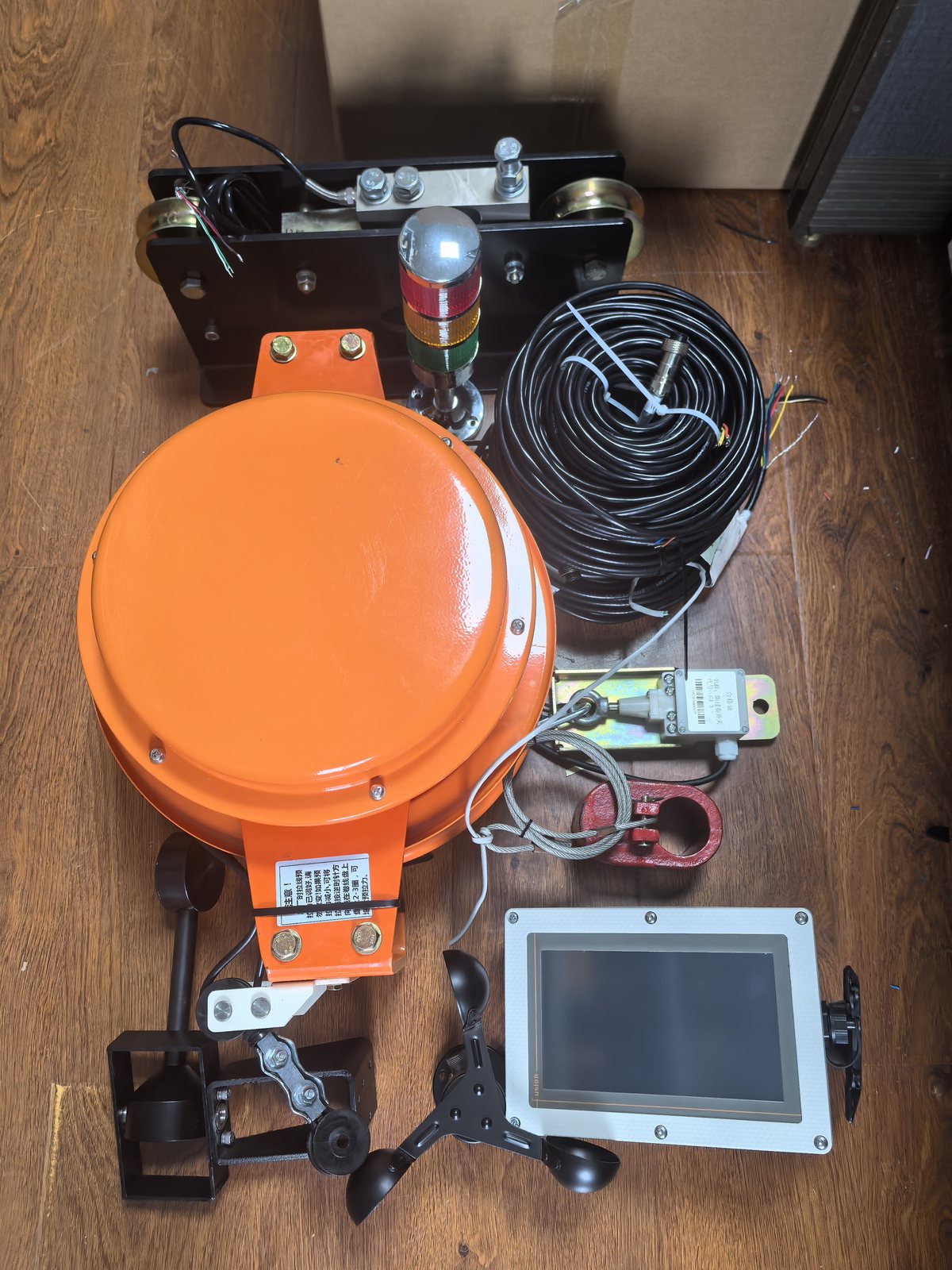 Orange draw-wire length sensor with terminal and accessory parts on a bench